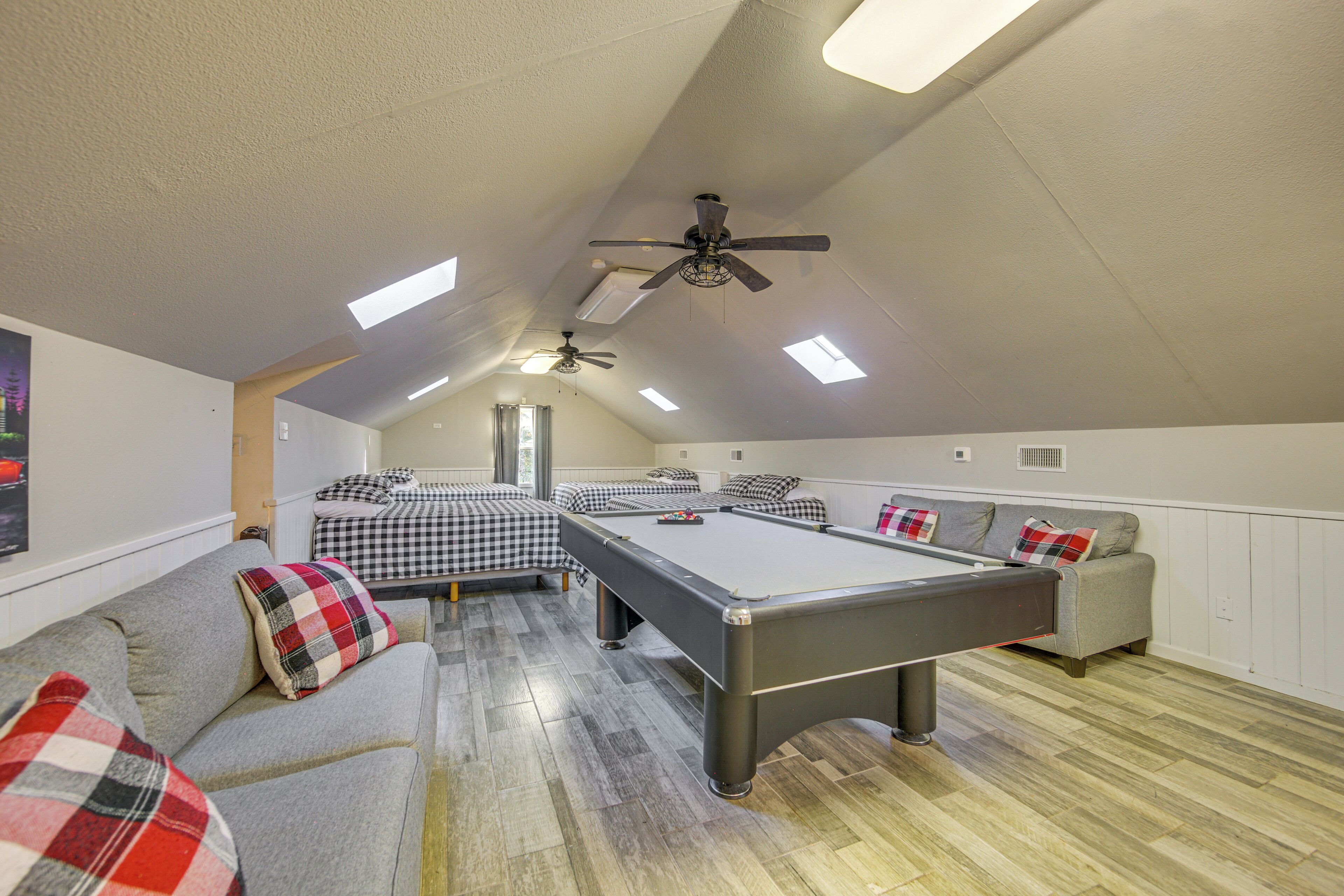 Een ruime kamer met een pooltafel, banken en plafondventilatoren.