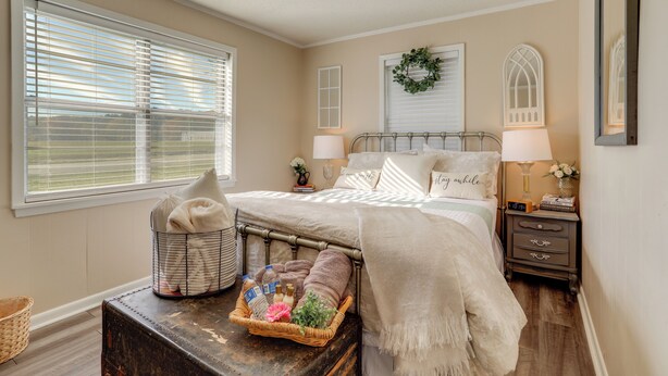 Een slaapkamer met een bed, nachtlampjes, een nachtkastje, een dressoir en een raam met jaloezieën.