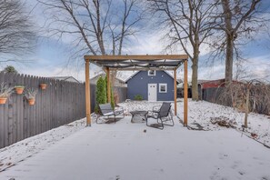 Un patio abrité avec une pergola en bois, deux chaises et une petite table.