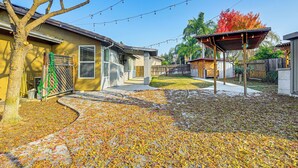 A residential backyard with a patio, string lights, a covered seating area, and a tree with autumn leaves. - 26 Mi to Fresno: Pet-friendly Home in Reedley! (Reedley)