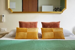 Une chambre d’hôtel avec un lit, deux oreillers, une couverture verte, un miroir fixé au mur et un thermostat.
