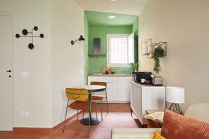 Eine kleine Küche mit Fenster, ein Essbereich mit Stühlen und eine gemütliche Sitzecke mit Sofa und Lampe.