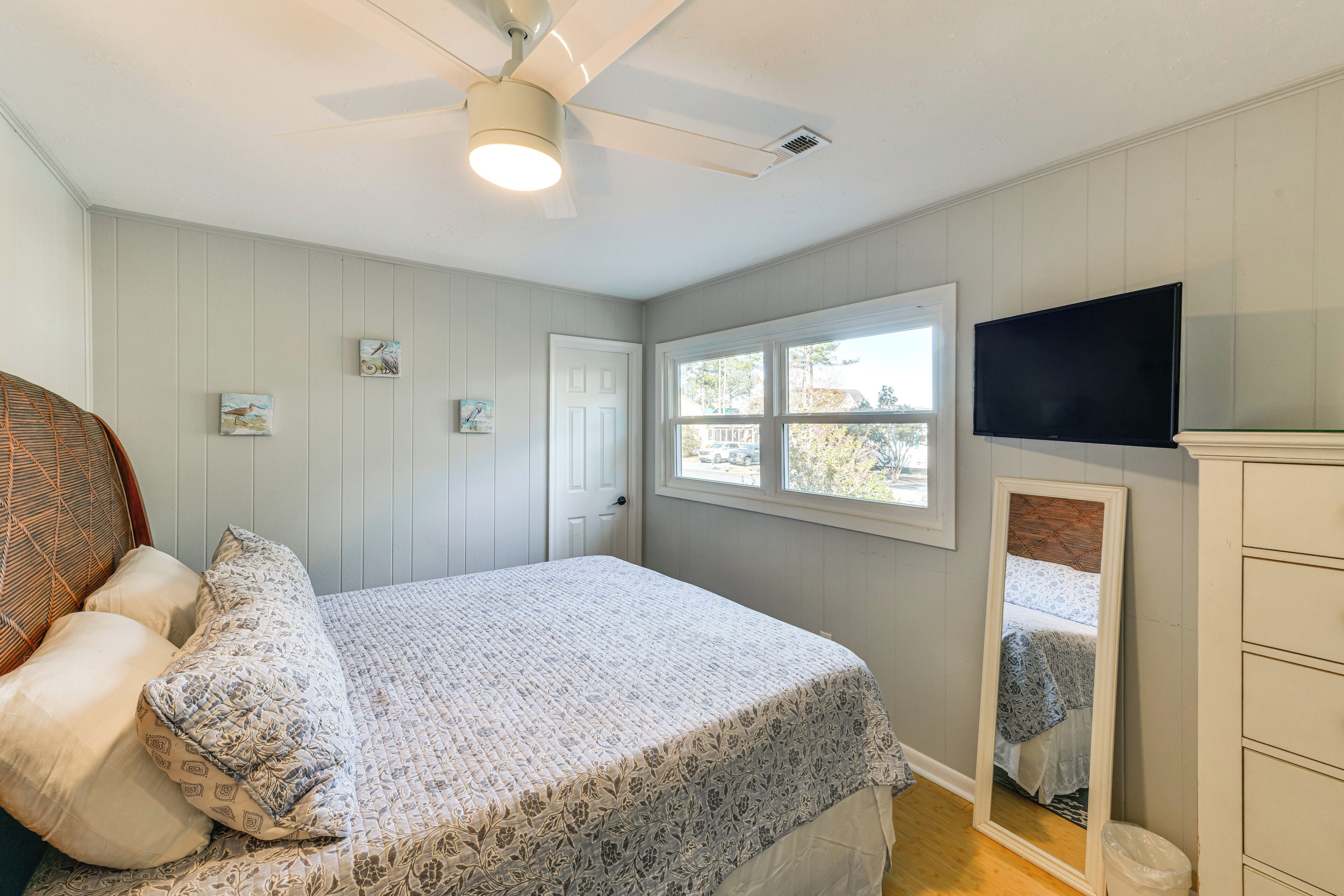 Un dormitorio con cama, ventilador de techo, ventana, televisor y cómoda.