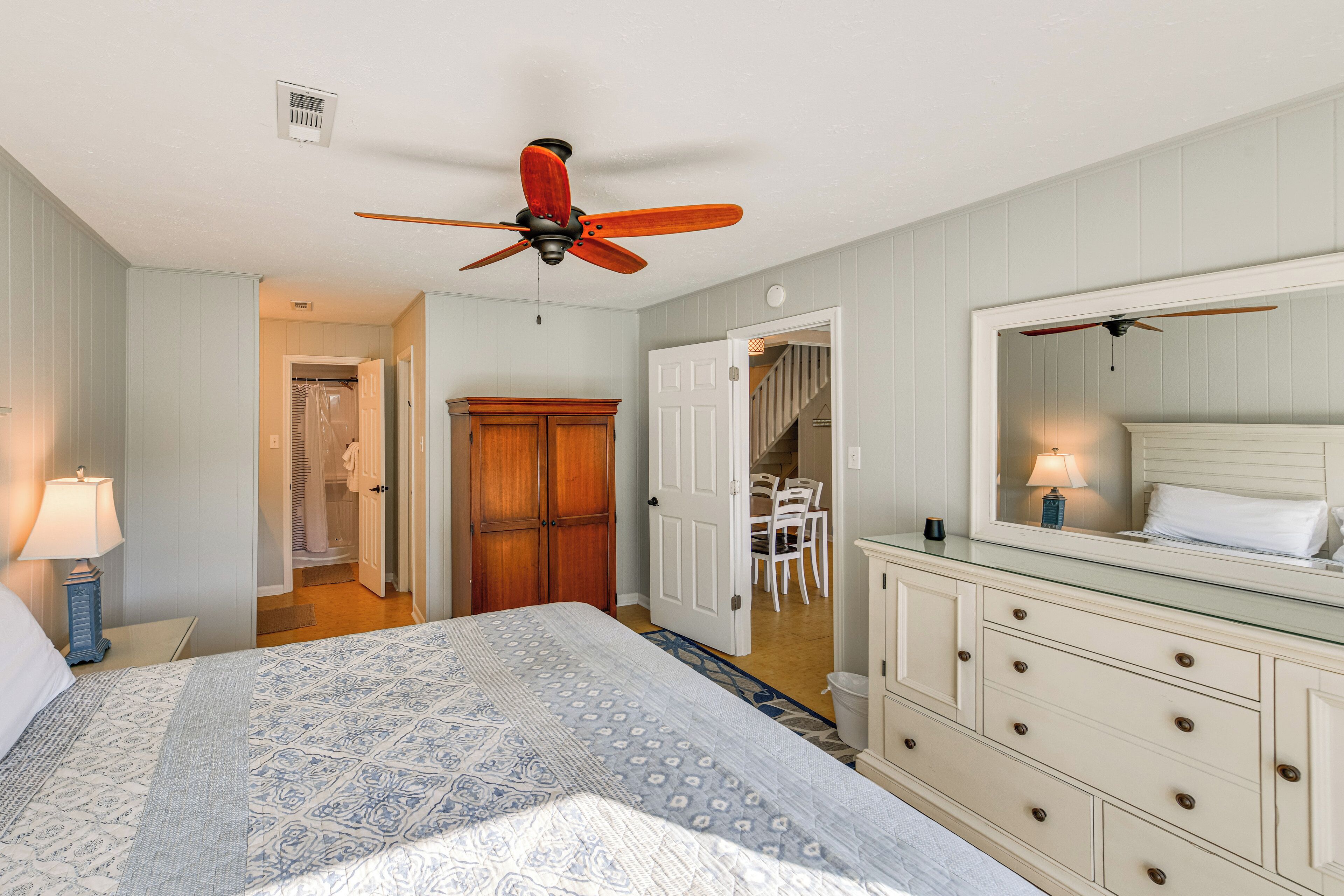 A bedroom with a bed, a dresser, a mirror, and a ceiling fan.