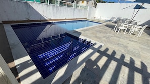 A swimming pool with a tiled deck, a metal ladder, and outdoor furniture.