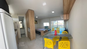 A modern kitchen with a glass dining table and yellow chairs, a wooden partition, and a view of the outside.