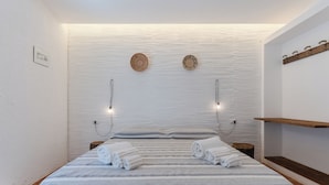 Un lit bien fait, avec une literie à rayures et deux serviettes enroulées, une tête de lit en bois et une étagère murale avec des crochets.