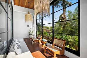 Une chambre moderne dotée de grandes fenêtres, d’un plafond en bois et d’un coin salon avec un canapé et des fauteuils.