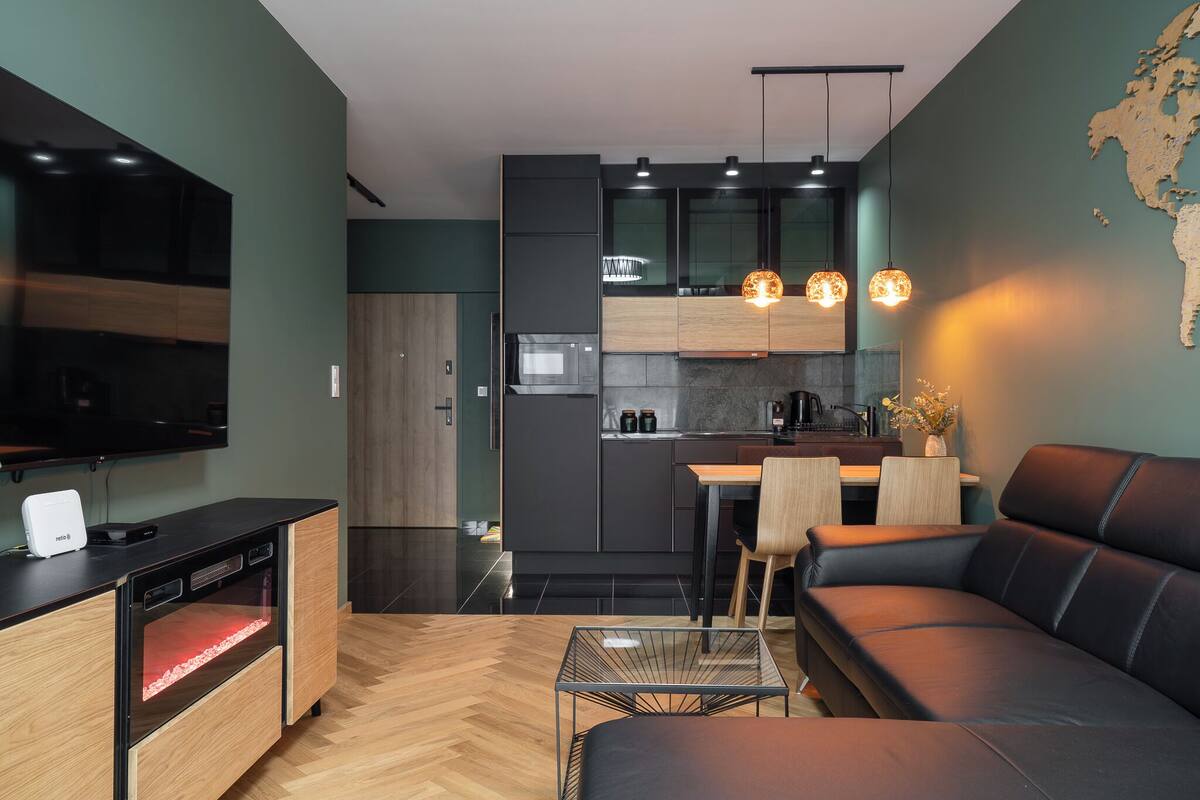 A modern kitchen with dark cabinetry, a microwave, and a dining area with a black leather sofa and a small table.