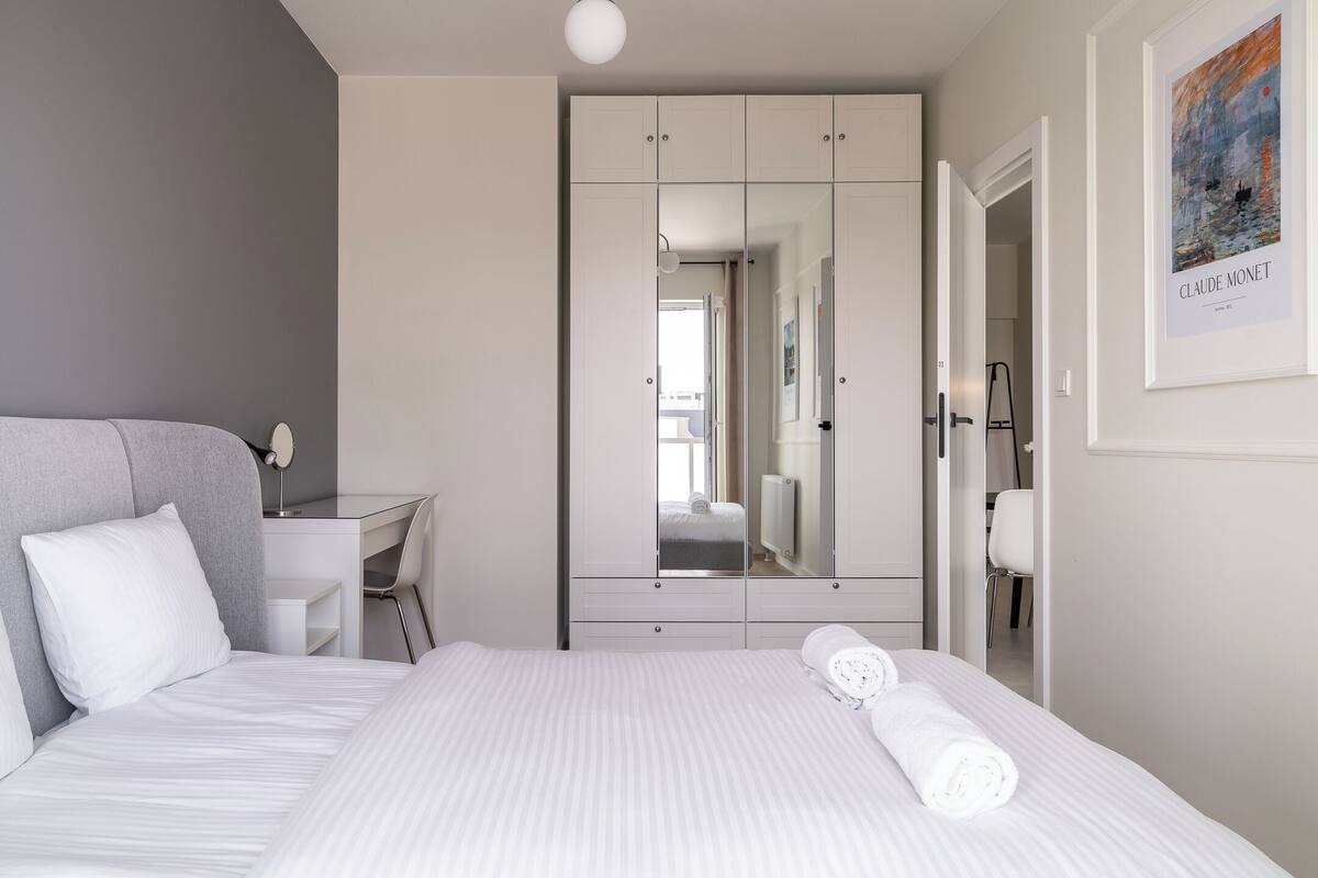 A modern hotel room with a large bed, a desk, and a wardrobe with a mirror.