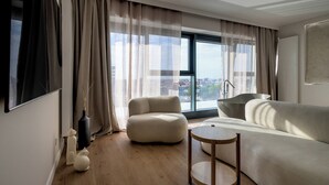 A modern living room with a sofa, a round wooden table, and a view of a cityscape through large windows. - RentPlanet - Apartamenty Quorum (Wroclaw)