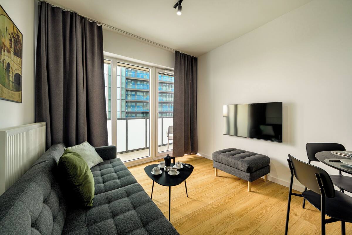 A modern living room with a sofa, ottoman, and a dining area with a table and chairs.