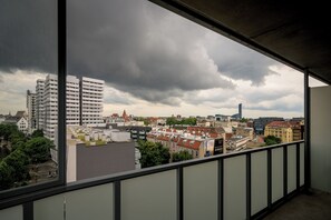 Näkymä parvekkeelta, josta avautuu kaupunkimaisema, jossa on näkyvissä erilaisia rakennuksia ja pilvinen taivas.