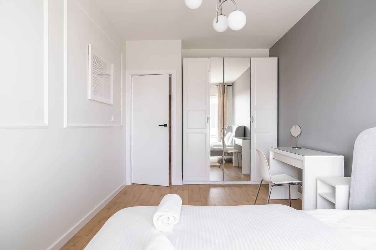 A modern hotel room with a neatly made bed, a desk with a chair, and a wardrobe.