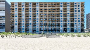 Ein mehrstöckiges Hotel mit einheitlicher Fassade, Balkonen und einem Sandstrand im Vordergrund.