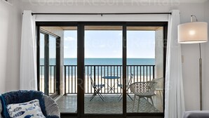 Ein Zimmer mit einer großen Schiebeglasdoor, die auf einen Balkon mit Meerblick führt. Auf dem Balkon befinden sich ein Stuhl und ein Tisch.