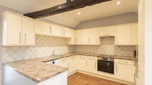 A kitchen with white cabinets, a granite countertop, a built-in oven, and a wooden floor. - Host Stay Croft Cottage (Malton)