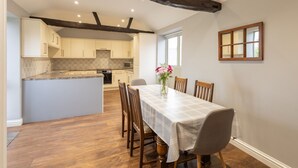 A spacious kitchen with a central island, wooden dining table with chairs, and a window with a view. - Host Stay Croft Cottage (Malton)