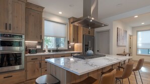 A modern kitchen with wooden cabinets, stainless steel appliances, a large island with bar stools, and a view of the outdoors. - cabin, hot tub! 3rd night free stay before 9/8/26 (Government Camp)