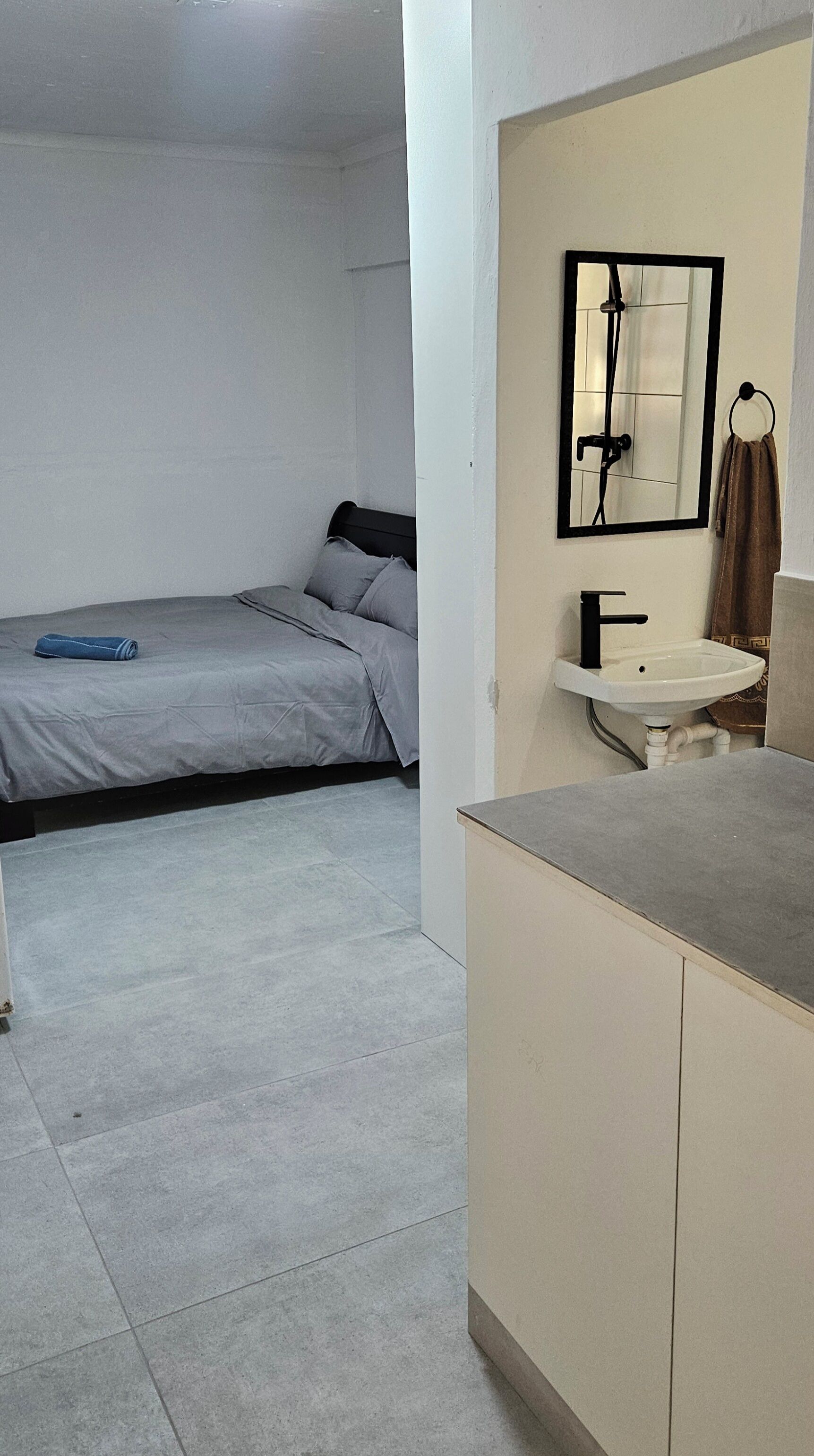 Una camera da letto con un letto, un bagno con lavandino e specchio, e un pavimento piastrellato.