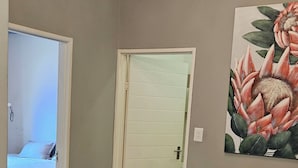 A room with a bed, a door, a painting, and a small table with stools.