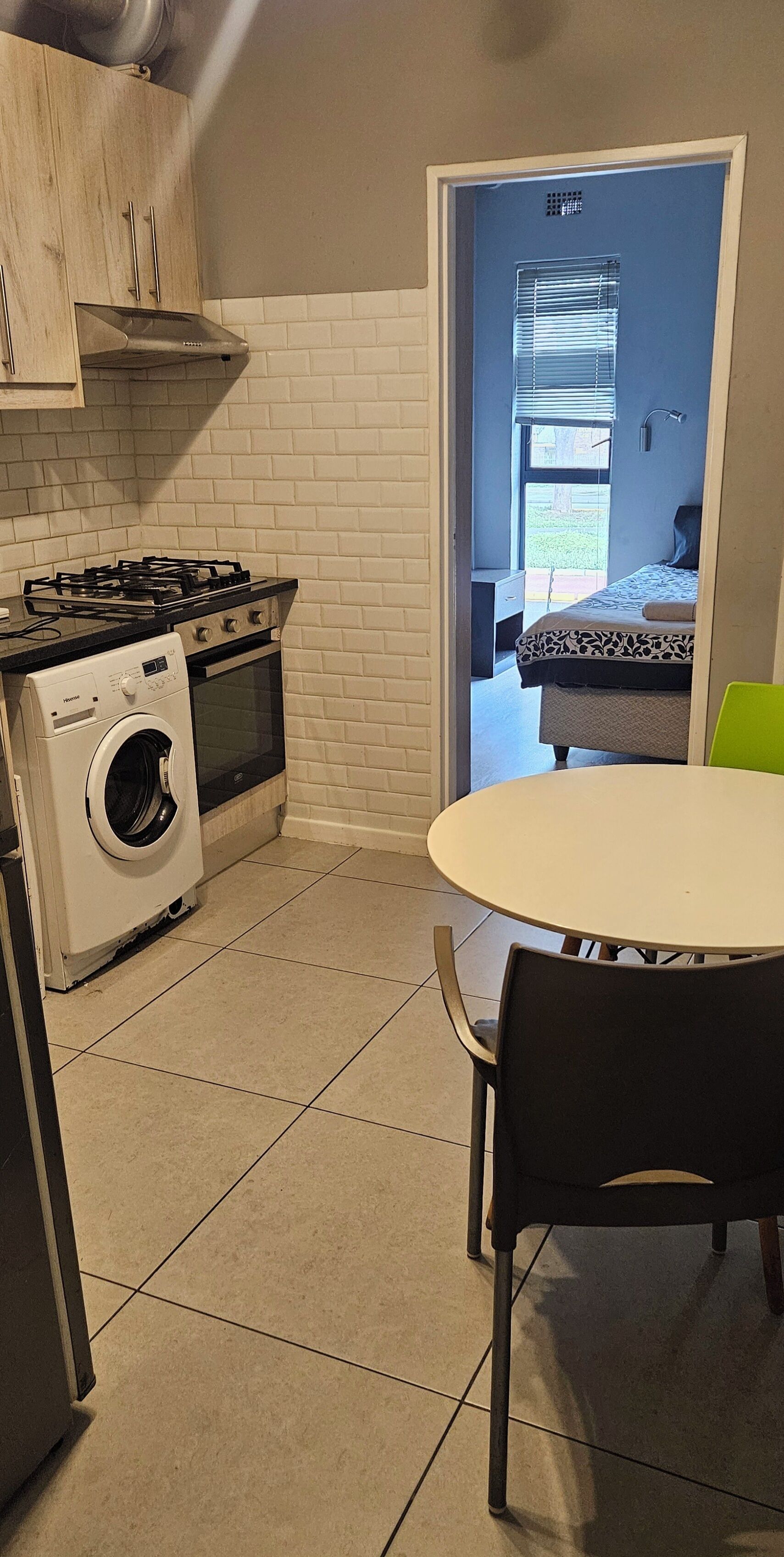 A compact kitchen with a gas stove, washing machine, and a dining area with a table and chairs.