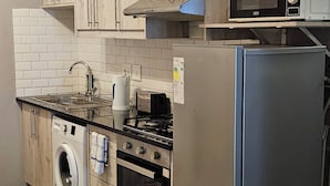 A kitchen with wooden cabinets, a stainless steel refrigerator, a microwave, a washing machine, and a stove.