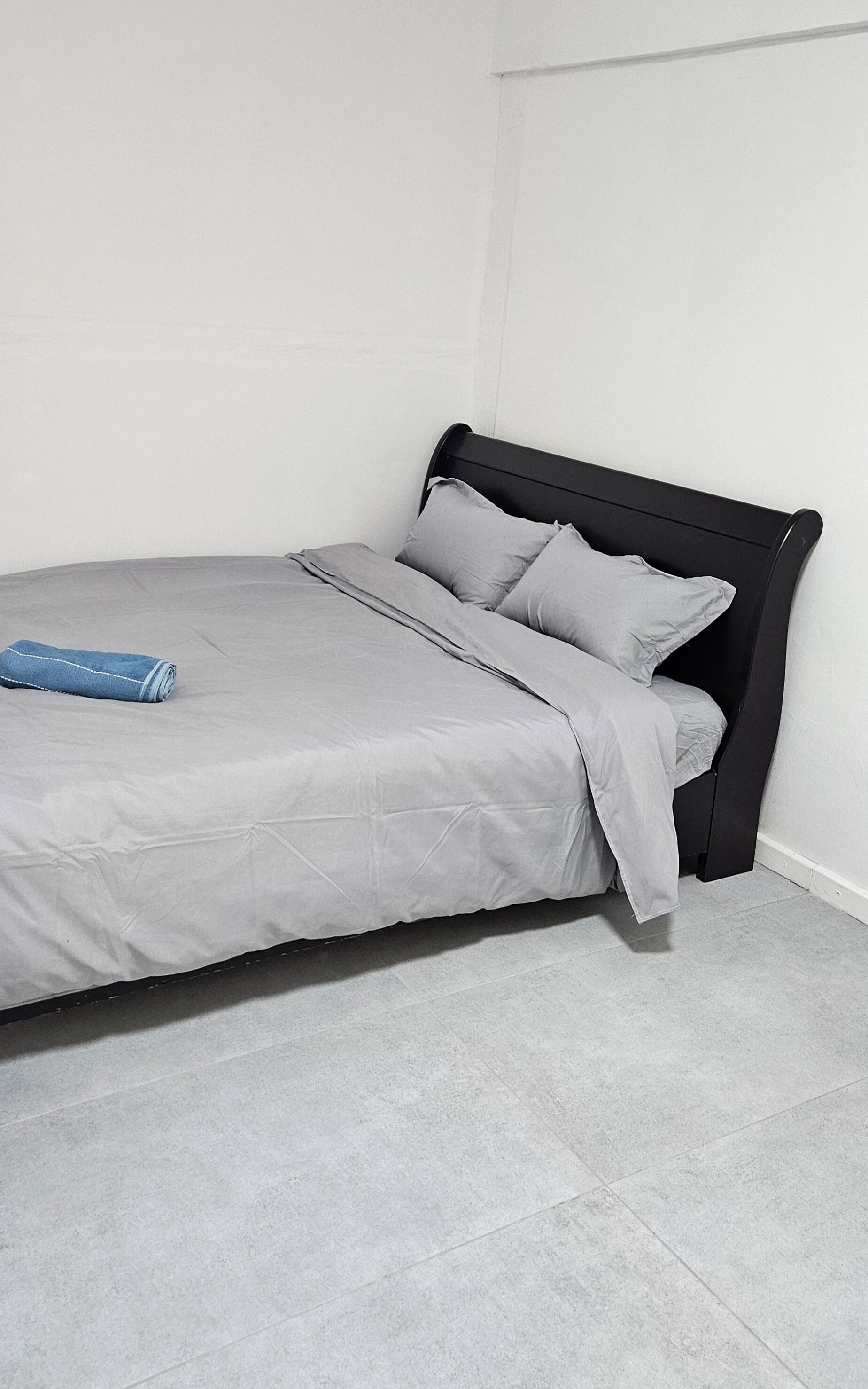 Un lit avec une tête de lit noire, une literie grise et une couverture bleue.