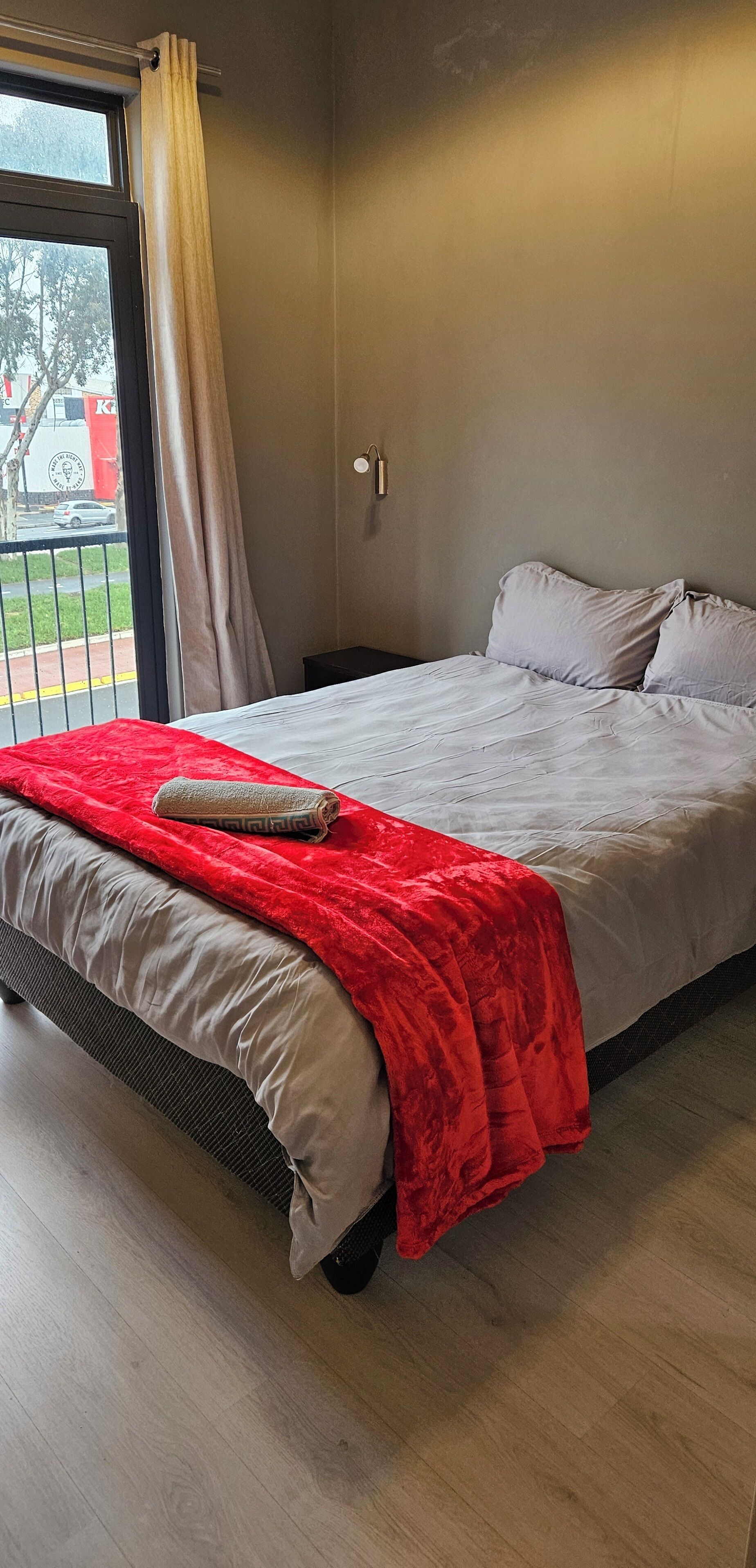 Quarto com cama, manta vermelha, janela com cortinas e vista para o exterior.