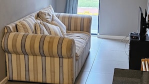 A living room with a striped sofa, a television, and a door leading to an outdoor area.