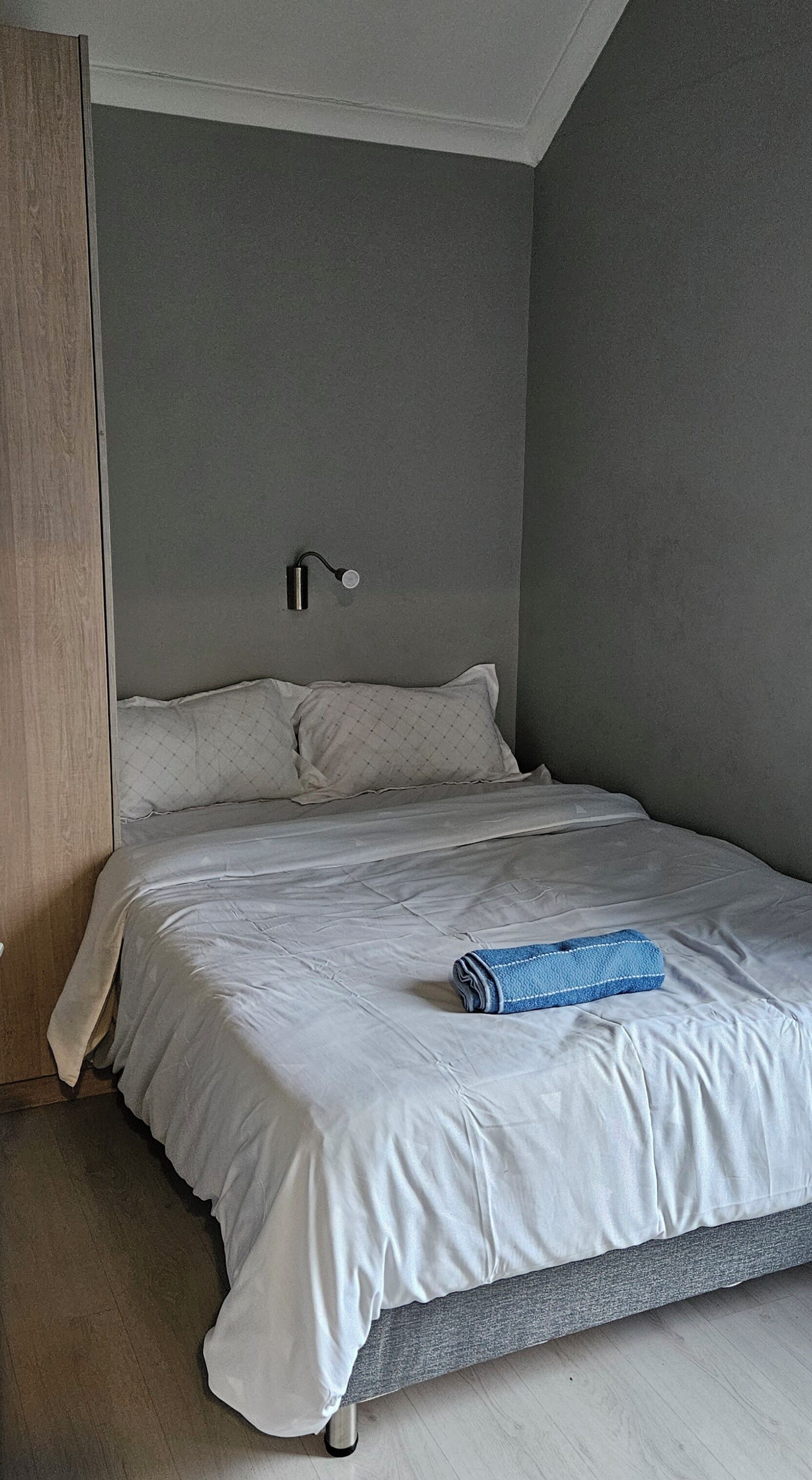 A bedroom with a bed, a wall-mounted light, and a wooden wardrobe.