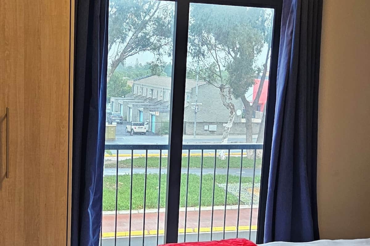 A hotel room with a bed, a window with curtains, a view of the outside, and a wooden wardrobe.