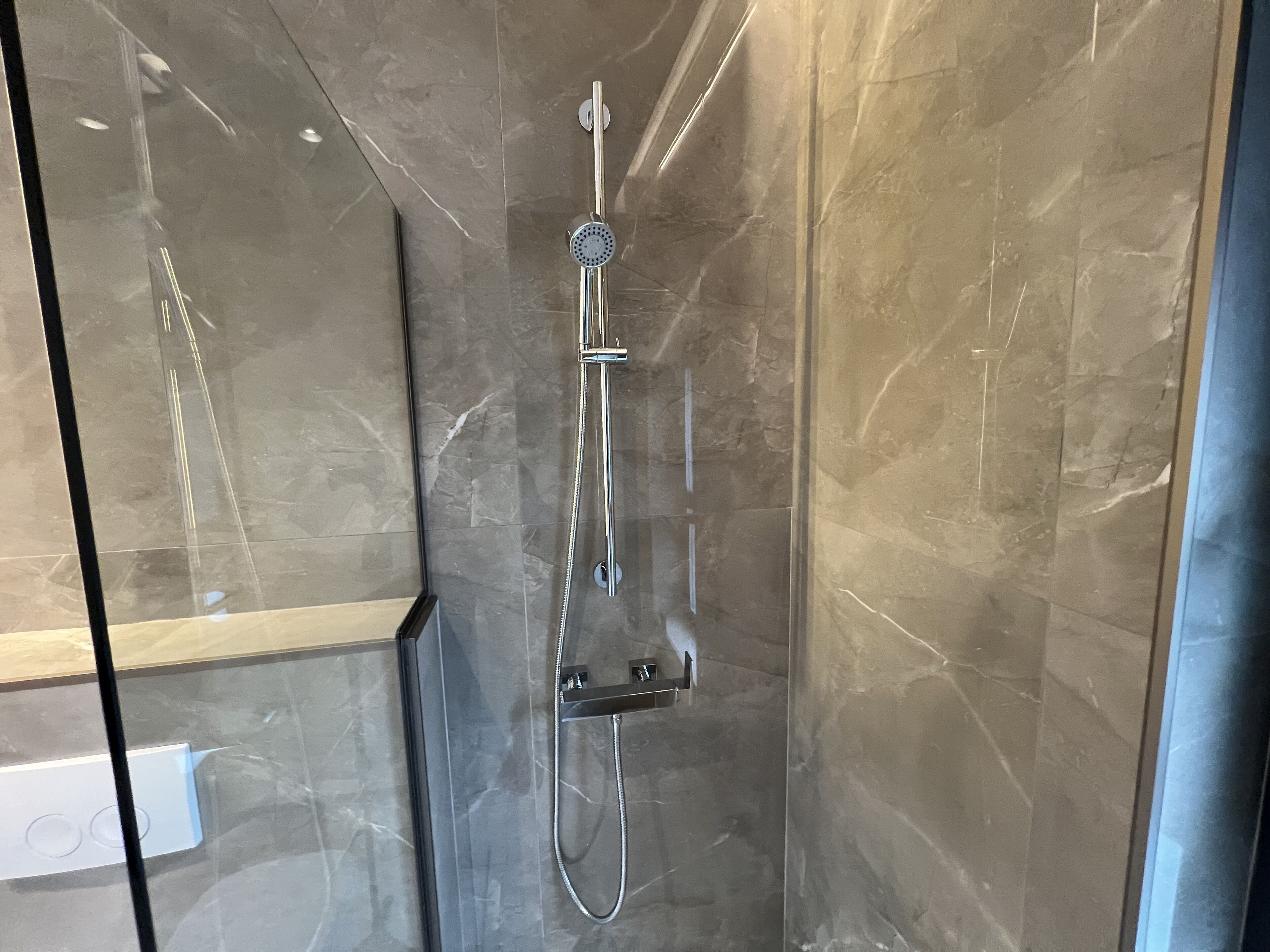 A modern shower with a handheld showerhead and a fixed rain showerhead, set against a marble wall.