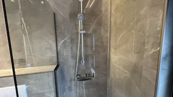 A modern shower with a handheld showerhead and a fixed rain showerhead, set against a marble wall.