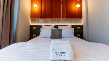Una camera d'albergo con un letto grande, due lampade ai comodini, una testiera illuminata e un letto rifatto con un asciugamano.