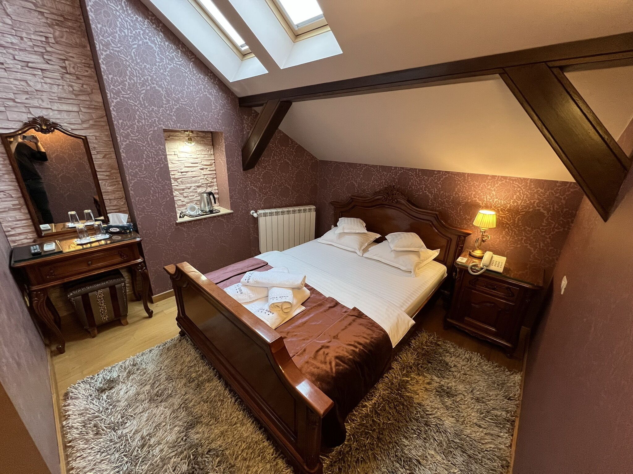 A bedroom with a sloped ceiling, a wooden bed, a nightstand with a lamp, a dresser, and a mirror.