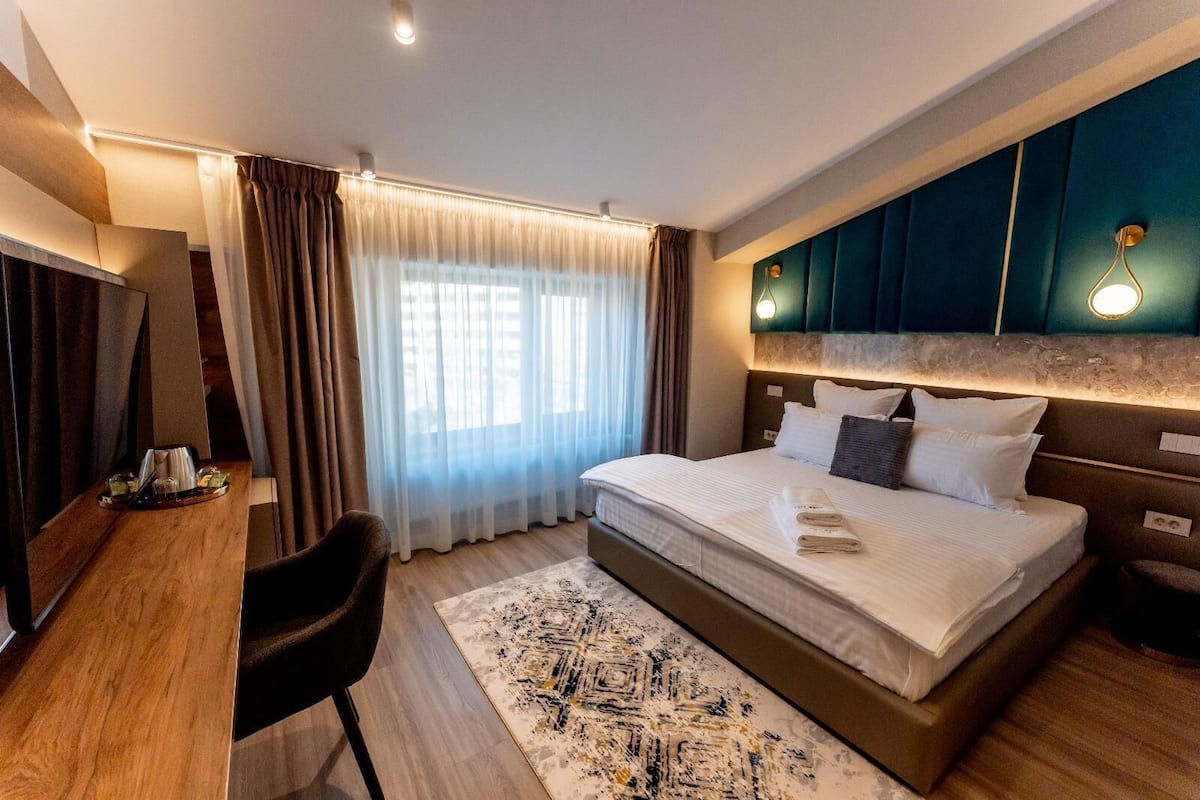A modern hotel room with a large bed, a desk, and a chair.