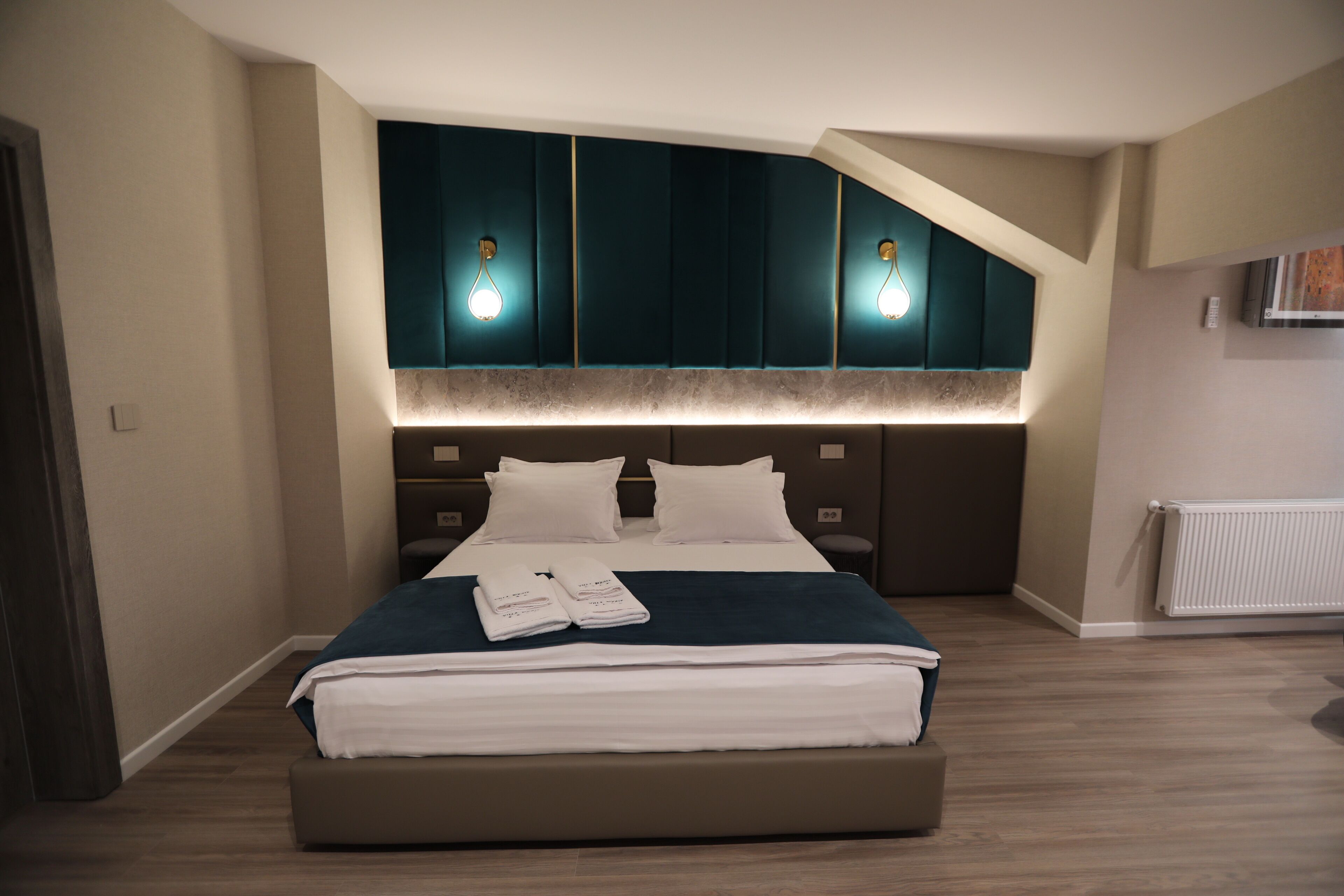 A modern bedroom with a large bed, dark headboard, and two wall-mounted lights.