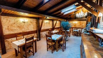 Ein Restaurant mit Holzbalken, Steinwänden und einem Kronleuchter. Die Tische sind mit weißen Tischdecken und Stühlen gedeckt.