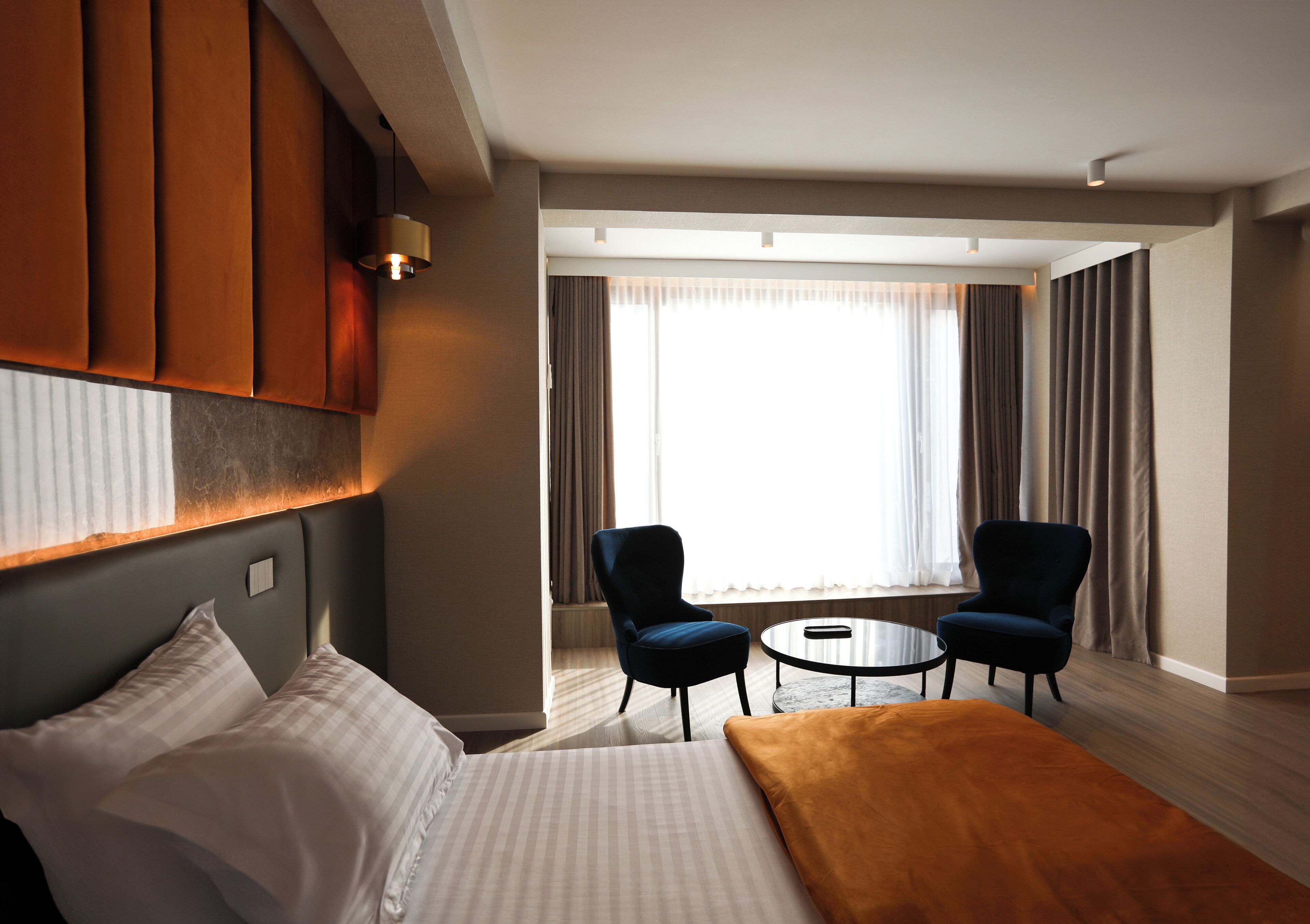 A hotel room with a bed, two armchairs, a small round table, and a large window with curtains.