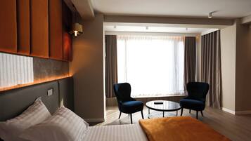 A hotel room with a bed, two armchairs, a small round table, and a large window with curtains.