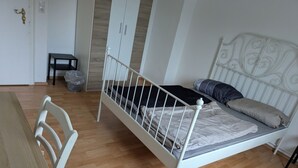 A bedroom with a wooden floor, a white bed with a headboard, a small table, and a chair. - NestOaseWHV Küstenzimmer im Stadtherz (Wilhelmshaven)