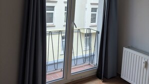 A room with a large sliding glass door leading to a balcony. The room has a wooden floor and a white radiator on the right. - NestOaseWHV Küstenzimmer im Stadtherz (Wilhelmshaven)