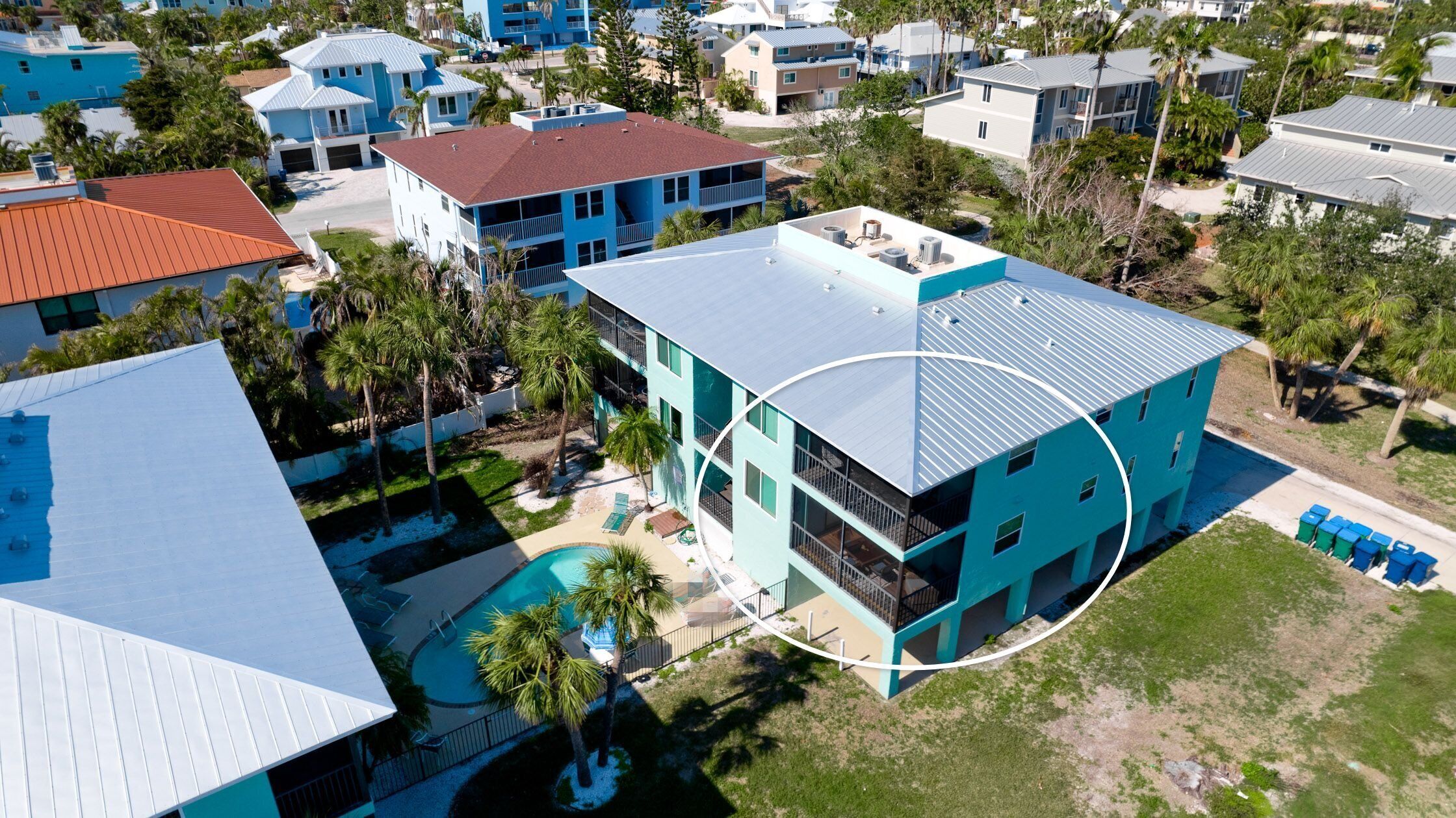 An aerial view of a residential area with modern houses, a swimming pool, and a large building with a blue roof.