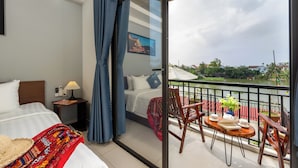 Ein Hotelzimmer mit Bett, Nachttisch, Lampe und einem Balkon mit Tisch, Stühlen und Blick auf einen Fluss.