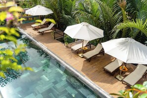 Ein Poolbereich mit Liegestühlen und Sonnenschirmen, umgeben von üppiger Vegetation.