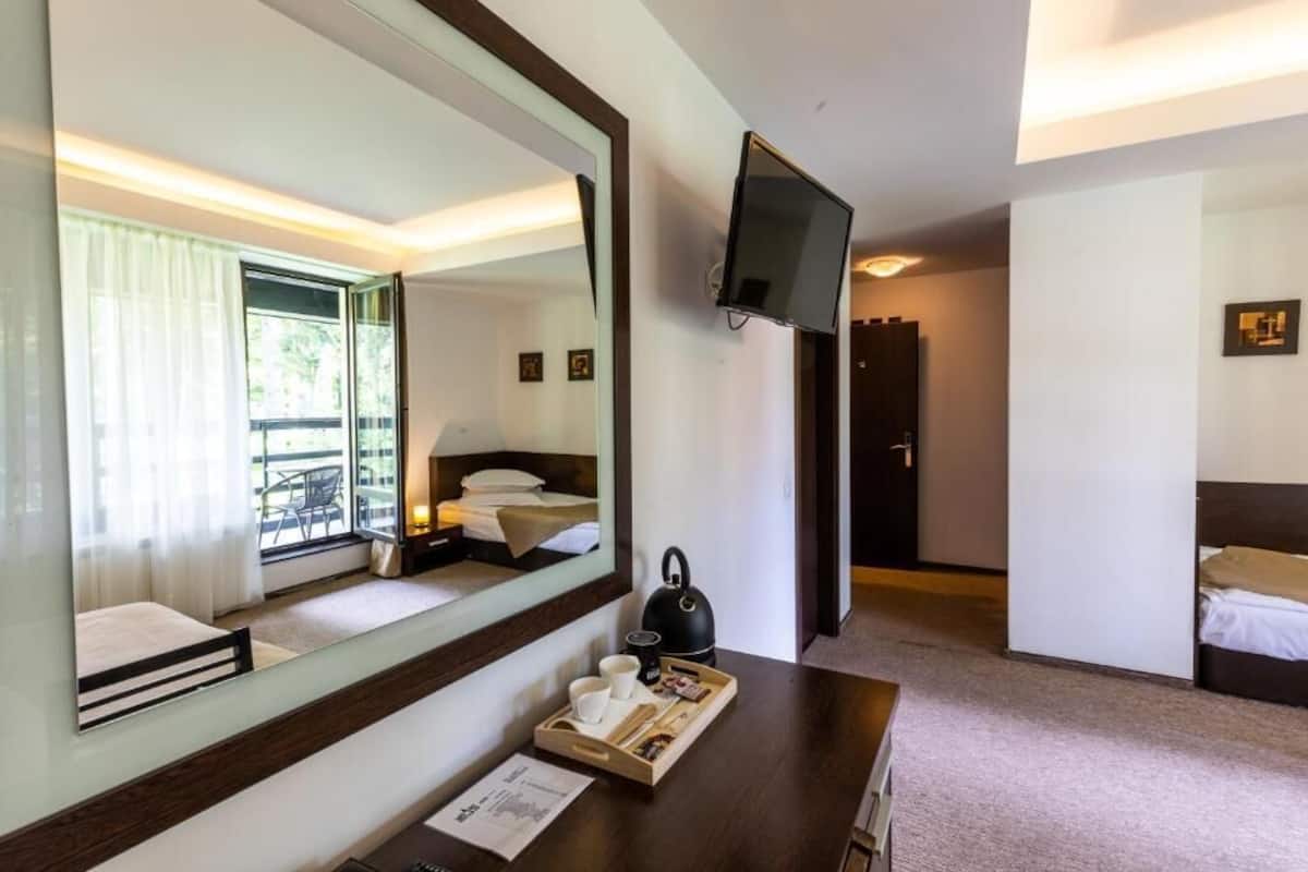 A hotel room with a large mirror, a flat-screen TV, a wooden desk with a tray of items, and a bed with a window view.