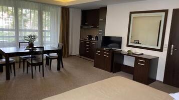 A hotel room with a bed, a desk with a chair, a television, a mirror, and a window with curtains.