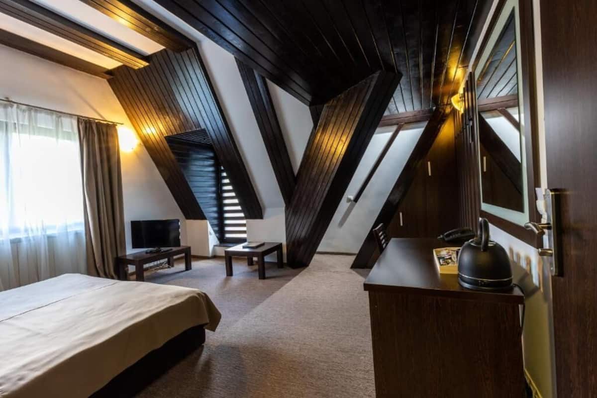 A hotel room with a large bed, a desk, a chair, a television, and a kettle.