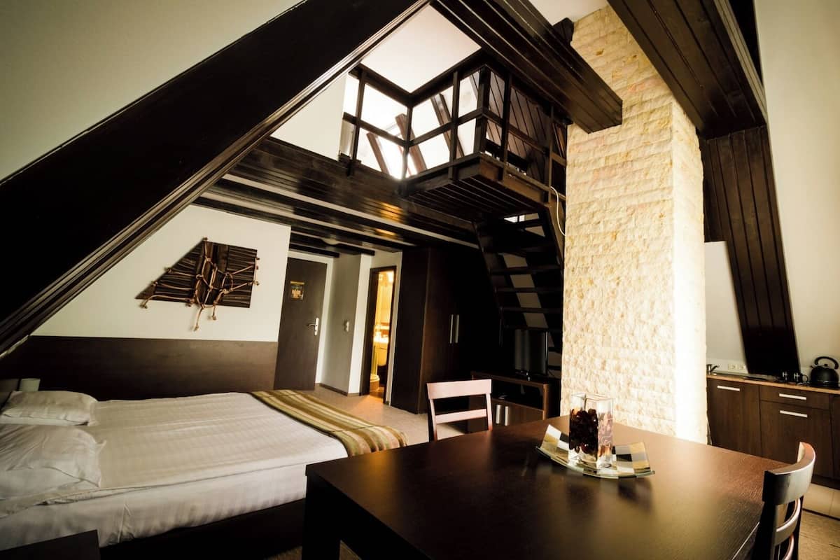 A bedroom with a sloped ceiling, a bed, a desk, and a chair.